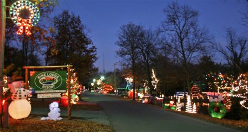 A festive street lined with colorful Christmas lights and decorations, leading to Pine Lodge Resort at dusk.