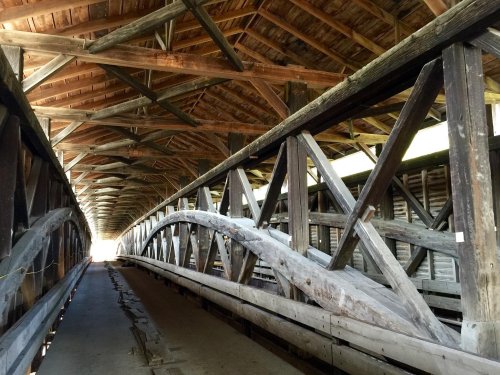 Interior view of a wooden covered bridge, showcasing its beams and structure, with light at the far end.