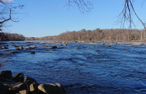 A serene river scene with rocky banks and trees lining the shore under a clear blue sky.