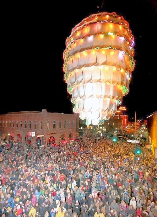 A large, illuminated ornament hangs above a massive crowd gathered in a festive street at night.