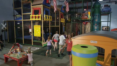 Children play in a colorful indoor playground with climbing structures, slides, and various activity areas.