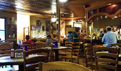 A cozy restaurant interior with wooden chairs, tables, and patrons enjoying their meals at the bar and dining area.