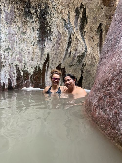 Two women relax in a natural pool surrounded by rocky cliffs, enjoying a serene moment together.