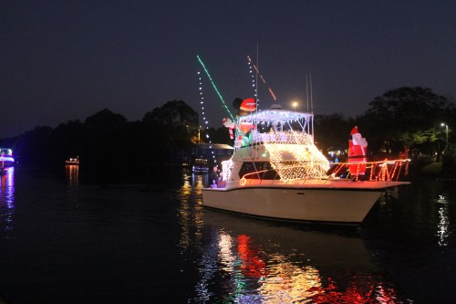 A decorated boat with colorful lights and festive ornaments sailing on a calm waterway at night.