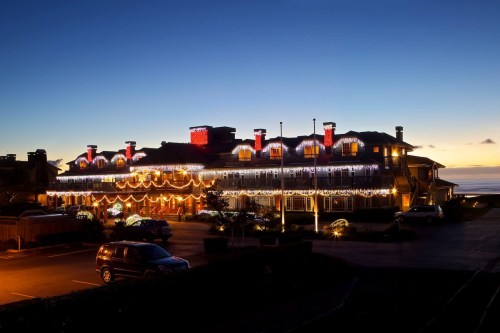 A beautifully lit hotel decorated with festive lights at dusk, overlooking the ocean.
