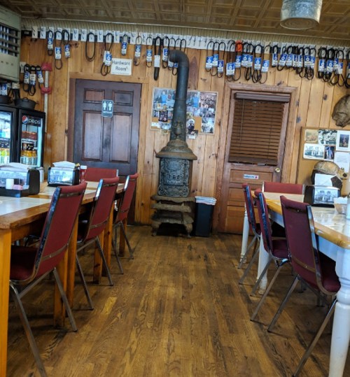 Cozy diner interior with wooden walls, tables, chairs, and a vintage stove, decorated with photos and memorabilia.