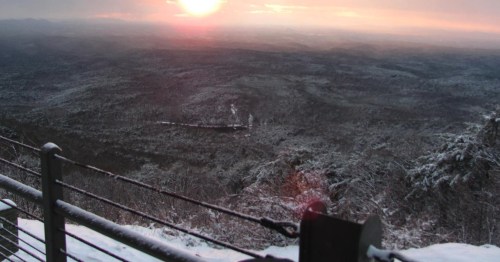 A snowy landscape at sunset, with mountains and a valley visible in the distance.