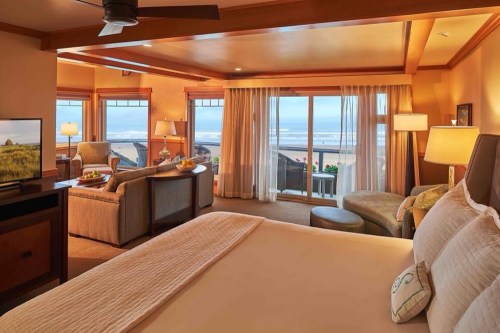 Cozy hotel room with a king bed, seating area, and large windows showcasing a view of the ocean.
