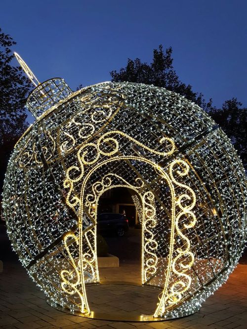 A large, illuminated Christmas ornament made of lights, set against a twilight sky.