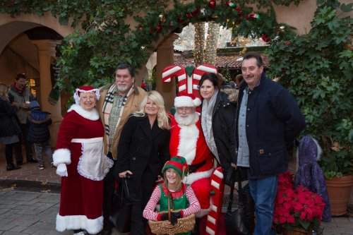 A festive group poses with Santa and an elf, surrounded by holiday decorations and greenery.