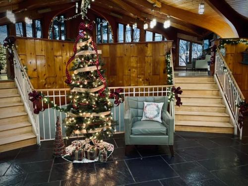 A beautifully decorated Christmas tree with lights and ribbons, next to a cozy chair in a festive indoor setting.