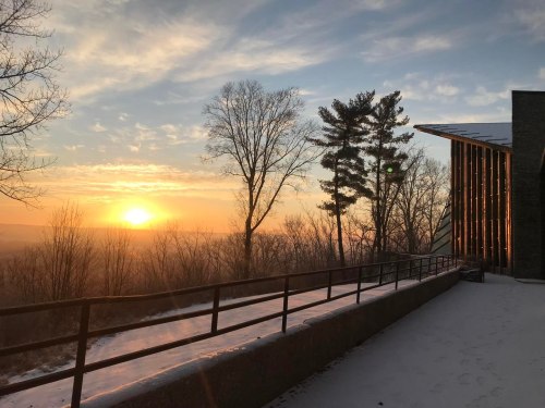Sunrise over a snowy landscape, with trees and a modern building silhouetted against a colorful sky.