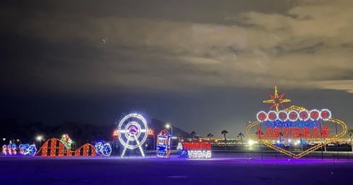 Colorful neon lights spelling "Las Vegas" and other attractions against a night sky, with mountains in the background.