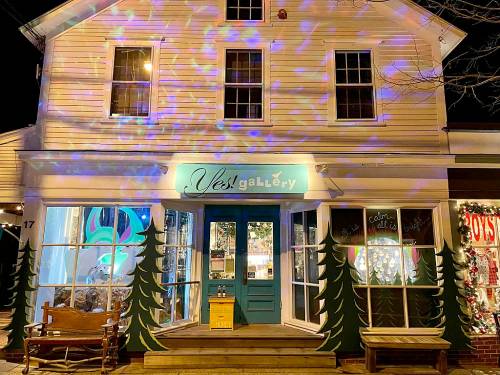 A brightly lit gallery at night, featuring colorful lights and festive decorations on the windows and entrance.