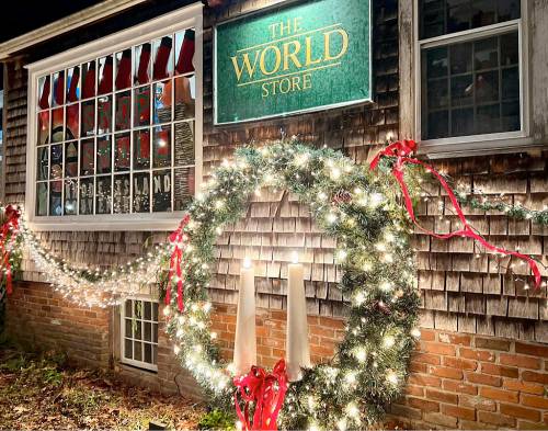 A festive storefront with a wreath, candles, and holiday lights, featuring a sign that reads "The World Store."