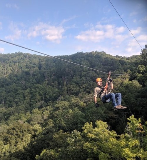 A person zip-lining through a lush green forest with a blue sky in the background.