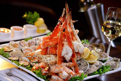 A lavish seafood platter featuring crab, shrimp, oysters, and lemon, garnished with lettuce and served with dipping sauces.