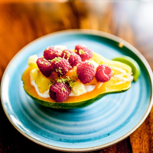 A vibrant dish featuring a halved papaya filled with yogurt, pineapple, and topped with fresh raspberries and mint.