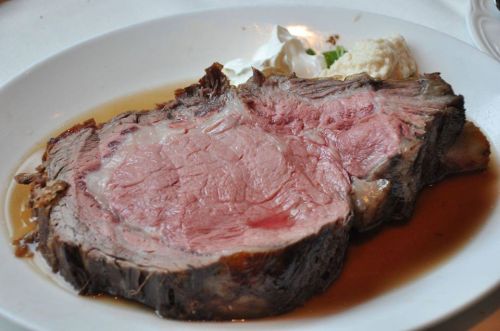 A juicy slice of prime rib served with a side of creamy horseradish sauce on a white plate.