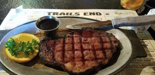 A grilled steak on a plate with a side of sauce, garnished with a slice of orange and parsley.