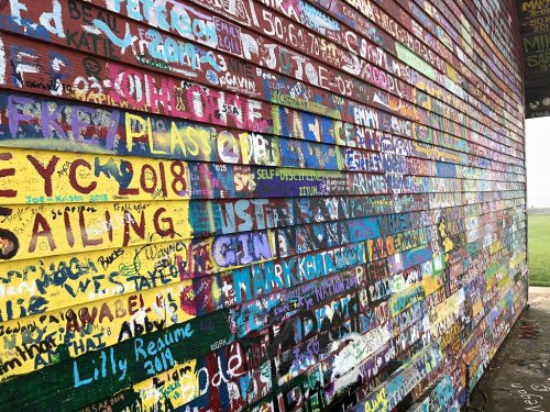 Colorful wall covered in graffiti and signatures, featuring various names, dates, and artistic designs.