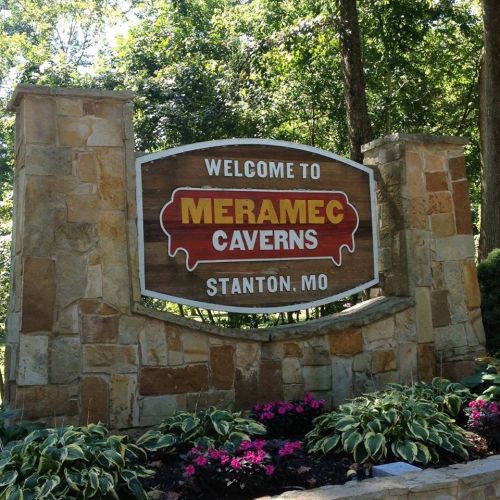Welcome sign for Meramec Caverns in Stanton, MO, surrounded by greenery and colorful flowers.