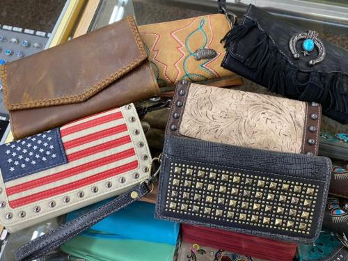 A collection of various stylish wallets and purses, featuring different designs and textures, displayed on a glass surface.