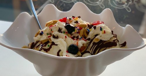 A bowl of ice cream topped with whipped cream, nuts, chocolate drizzle, and colorful sprinkles.