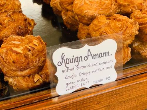 A display of kouign amann pastries with a sign describing them as salted caramelized croissant dough, crispy and gooey.