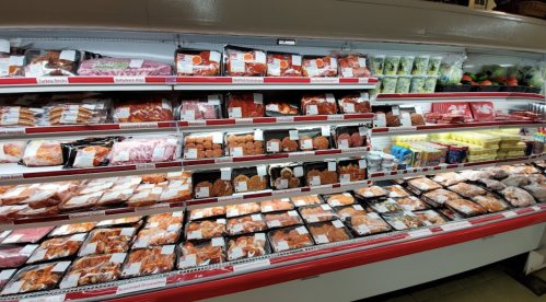 A well-stocked meat display in a grocery store, featuring various packaged meats and seafood on shelves.
