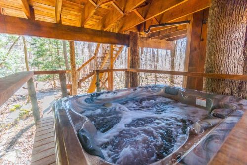 A hot tub on a wooden deck surrounded by trees, with a staircase leading up in the background.