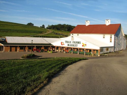 A scenic view of Trax Farms Market, featuring a large white building with a red roof and green fields in the background.