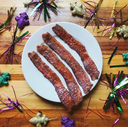 A plate of crispy bacon strips surrounded by colorful festive decorations on a wooden surface.