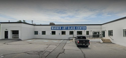 Exterior of Warner Art Glass Center, featuring a white building with blue signage and a parking lot.