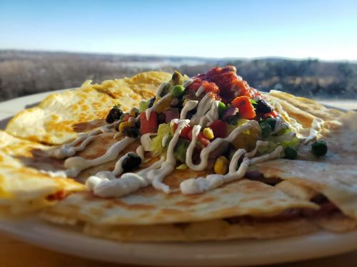 A plate of quesadillas topped with salsa, sour cream, and fresh vegetables, with a scenic view in the background.