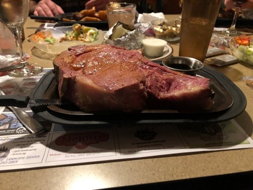 A large, juicy prime rib served on a sizzling platter, accompanied by a small bowl of sauce.
