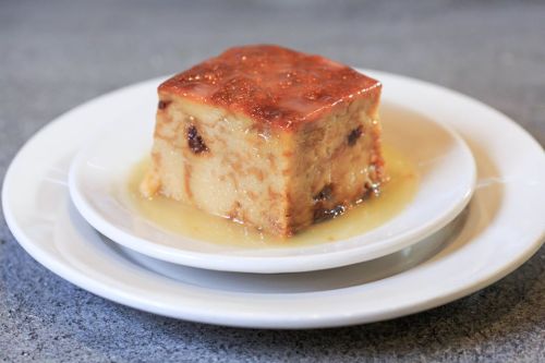 A square slice of bread pudding drizzled with a golden caramel sauce on a white plate.