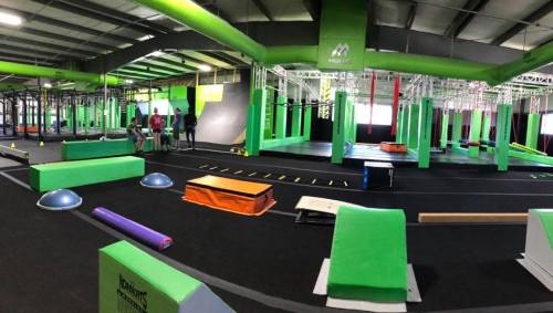 A vibrant indoor gym with green walls, various obstacle courses, and people engaging in activities.