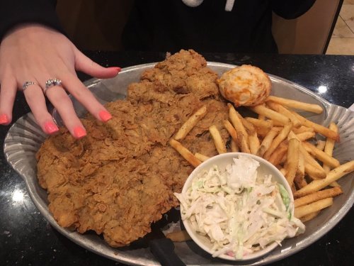 A large platter of fried chicken, French fries, coleslaw, and a biscuit, with a hand showing brightly painted nails.
