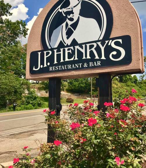 Sign for J.P. Henry's Restaurant & Bar, surrounded by blooming flowers and a clear blue sky.