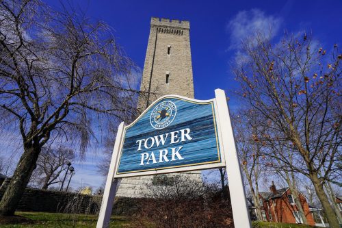 Sign for Tower Park in front of a tall stone tower, with trees and a blue sky in the background.