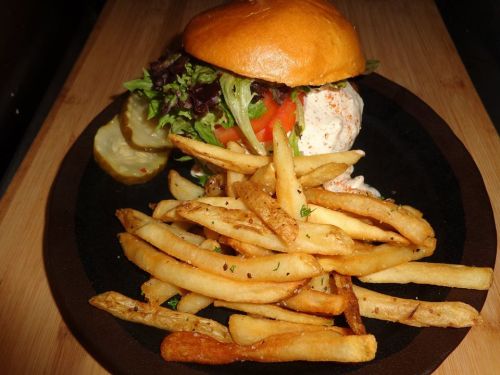 A delicious burger with lettuce, tomato, and sauce, served with crispy French fries and a pickle on the side.