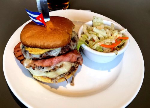 A Cuban sandwich with layers of meat and cheese, topped with a flag, served with a side of coleslaw.