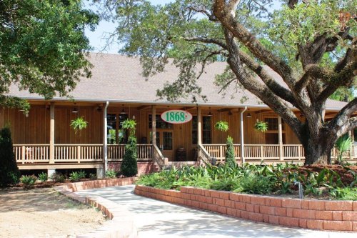 A wooden building with a sign reading "1868," surrounded by greenery and trees on a sunny day.