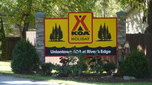 Sign for Uniontown KOA Holiday at River's Edge, featuring trees and decorative plants.