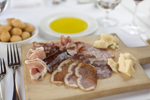 A wooden platter with assorted cured meats and cheese, accompanied by a small bowl of olive oil and bread rolls.