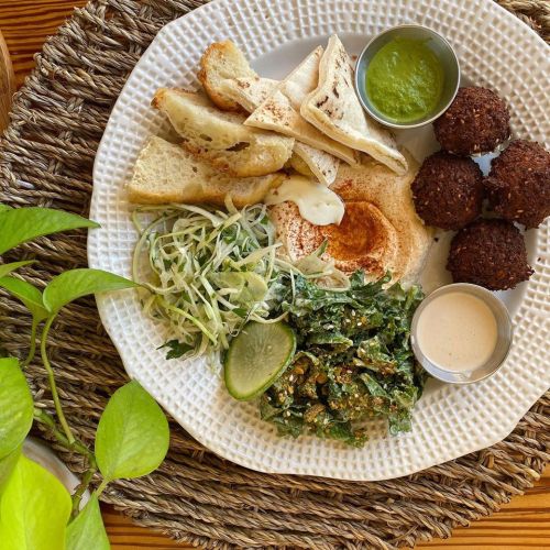 A plate with pita bread, falafel, salad, and sauces, arranged on a textured white plate with a woven placemat.