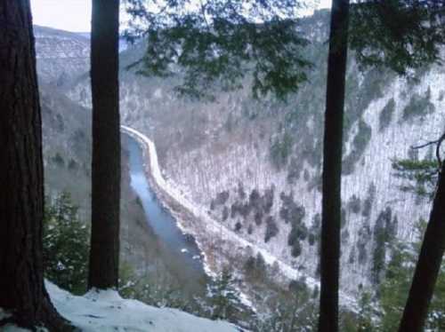 A scenic view of a winding river surrounded by snow-covered hills and tall trees.