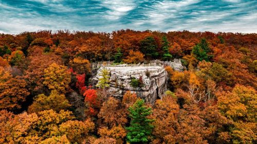 A rocky outcrop surrounded by vibrant autumn foliage under a cloudy sky.
