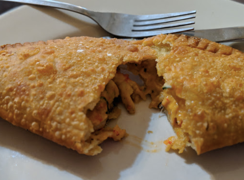 A golden, flaky pastry filled with colorful vegetables, partially cut open on a white plate with a fork and knife.